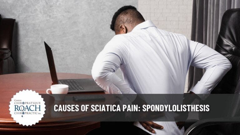 Causes of Sciatica Pain: Spondylolisthesis 4 a man sitting at a table holding his lower back, experiencing spondylolisthesis